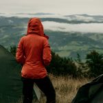 Back view of girl tourist in orange jacket looking at beautiful scenery of mountains